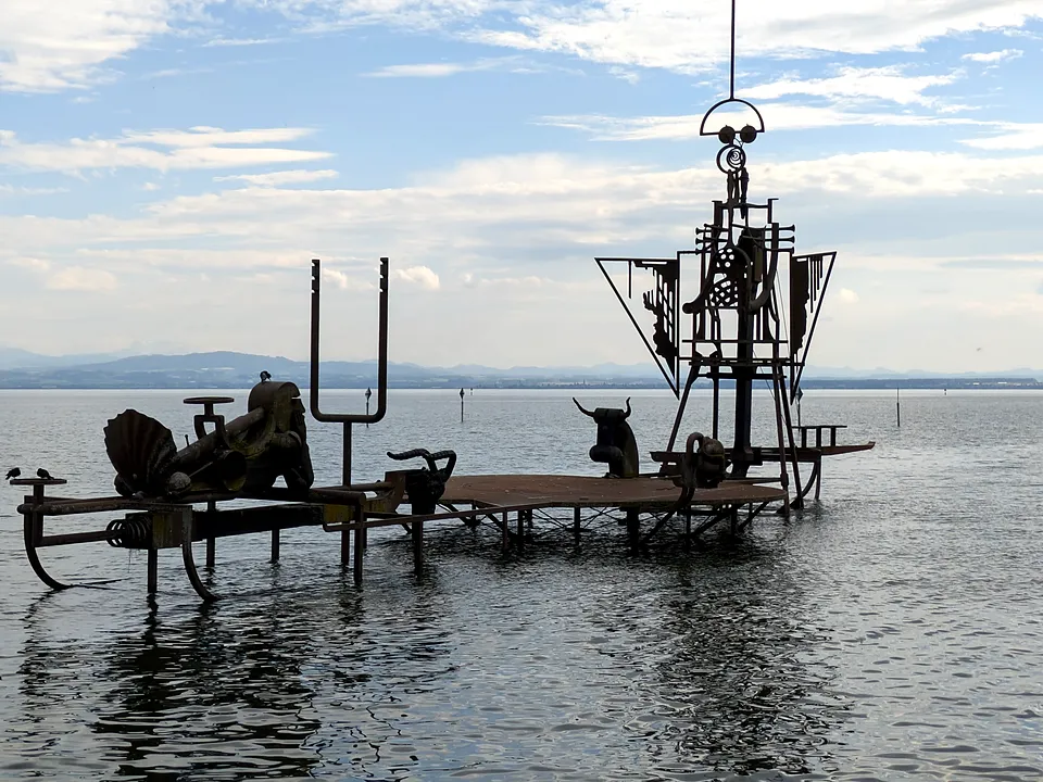 Skulptur im Wasser vor Friedrichshafen, dahinter der See und die Berge am anderen Ufer