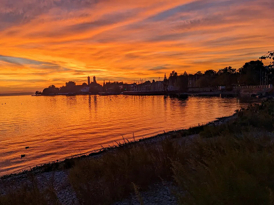 Sonnenuntergang über dem See bei Friedrichshafen, am Ufer eine Silhouette der Stadt