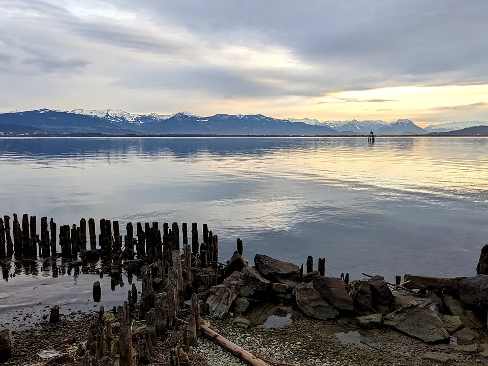 Ufer bei Lindau mit Holzpfählen im flachen Wasser und Bergen am Horizont